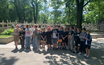Powiększ obraz: uczniowie stoja na tle brzozowych krzyzy na Cmentarzu Powazkowskim